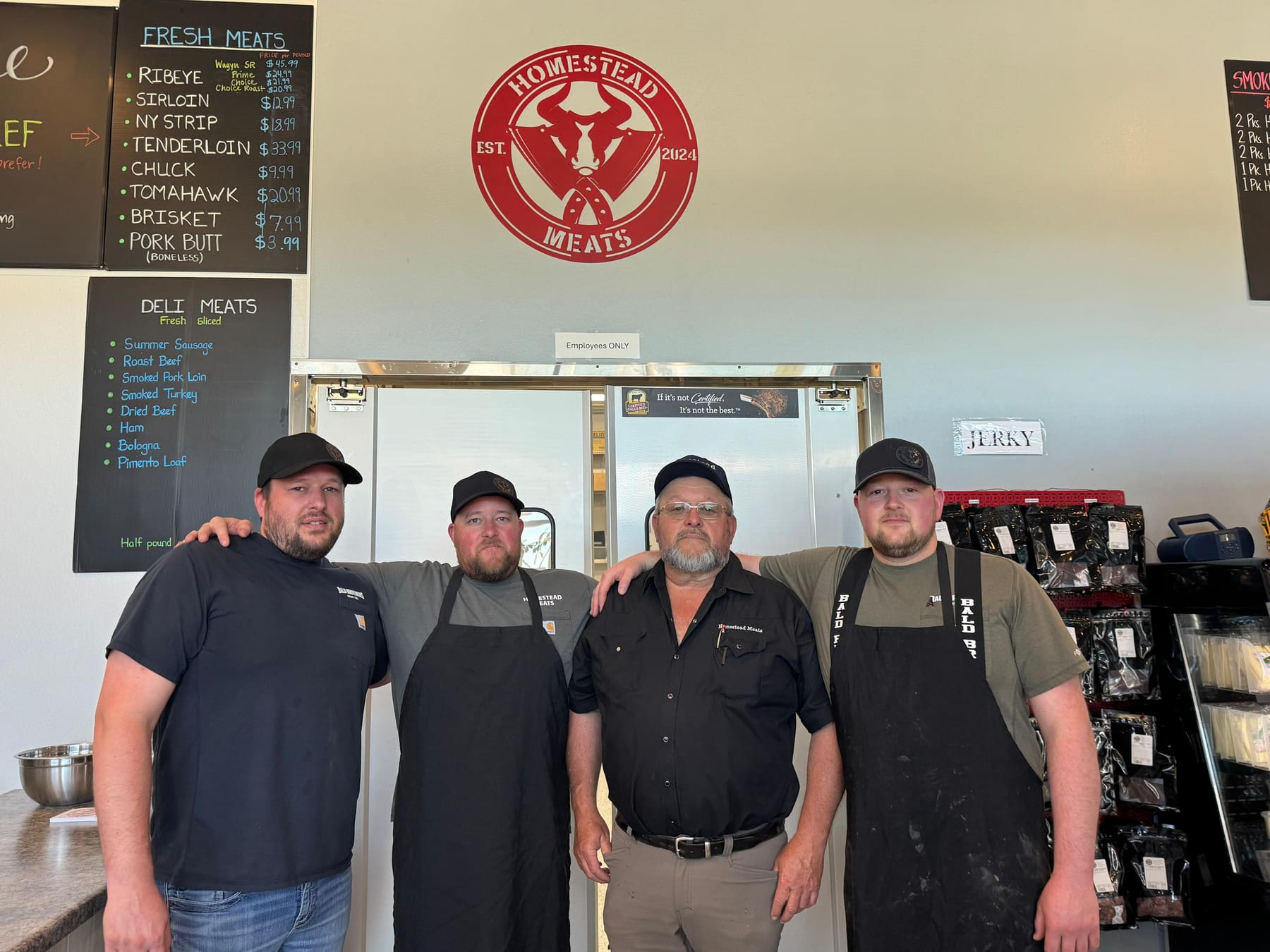 The Bald Brothers family behind the counter at Homestead Meats, under the shop's red logo and chalkboard menus